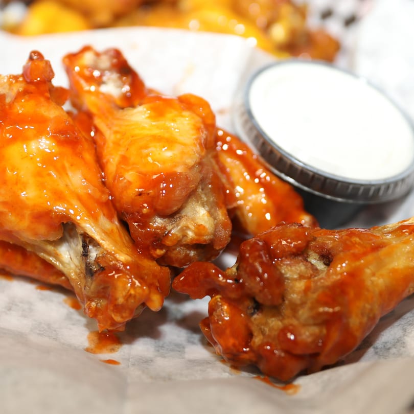 Close-up of Tj Pizza's buffalo chicken wings with ranch dressing in a plastic cup.