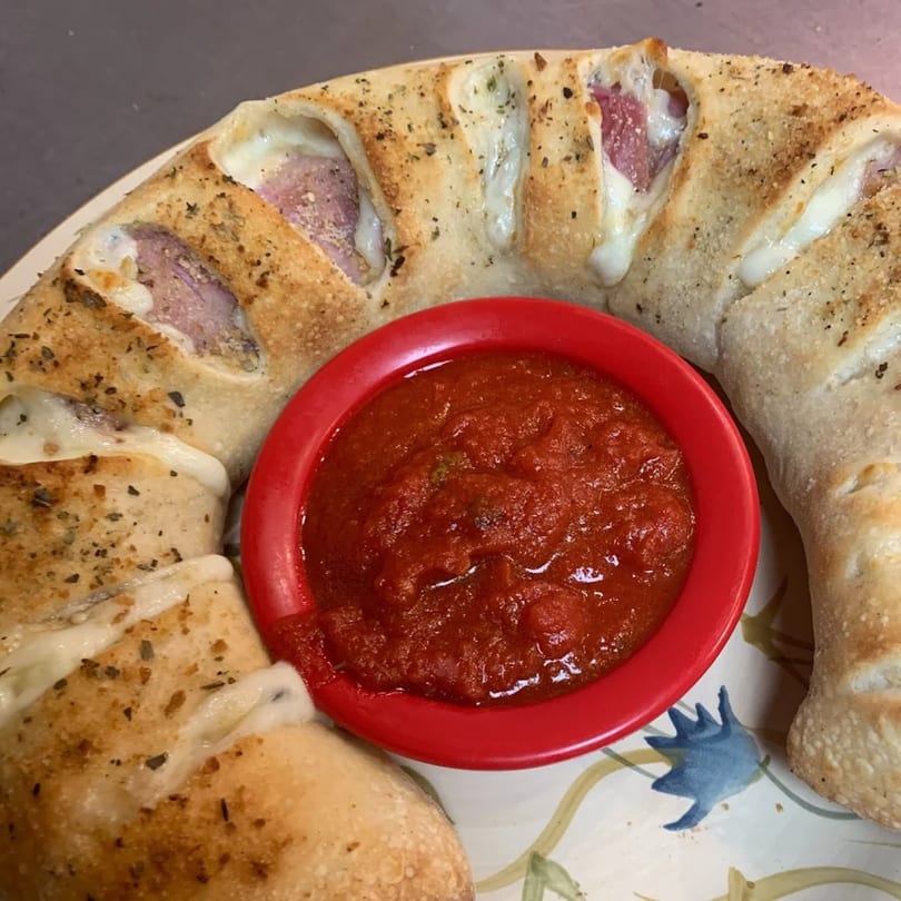 A golden-brown calzone filled with meat and cheese, served with a side of red marinara sauce.